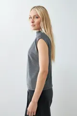 Blusa plateada de lurex con cuello alto y tablas en los hombros. Sin mangas.
