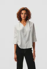 Camisa blanca de algodón con cuello camisero, corte holgado, mangas 3/4 y cierre frontal con botones.