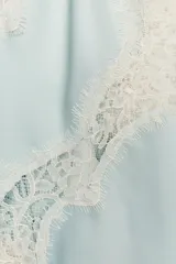 Top lencero celeste con escote en V, tirantes finos y detalle de encaje blanco en el escote y el ruedo asimétrico.