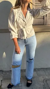 Pantalón de jean celeste de corte recto con roturas en las rodillas y detalles de crochet artesanal y pedrería en la parte trasera.