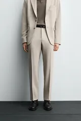 Pantalón de vestir color beige, corte slim fit, confeccionado en tejido con viscosa. Cuenta con bolsillos frontales y traseros de doble vivo con botón. Cierre frontal con cremallera y botón.