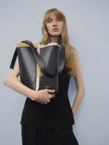 Bolso tipo tote de cuero negro con detalles en beige y correa larga ajustable con hebilla metálica.