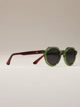 Lentes de sol con montura octogonal de acetato verde y patillas de acetato marrón con detalle naranja en el extremo. Lentes de color negro.