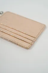 Tarjetero metálico color plateado con textura rugosa y costuras visibles. Incluye una pequeña etiqueta de marca en la parte superior.