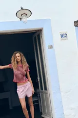 Camiseta de punto con rayas horizontales en tonos rosa, marrón y beige. Tiene cuello redondo con ribete y mangas cortas con volantes en los extremos.