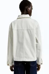 Campera color crudo en sarga de algodón con cuello, botones adelante y canesú en la espalda. Modelo de hombros apenas caídos con bolsillos superiores de parche, bolsillos insertados adelante y puños abotonados.