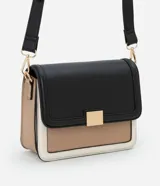 Cartera mediana de PU color negro, con asa transversal regulable, detalle metálico dorado en el frente y recortes contrastantes en beige y blanco.