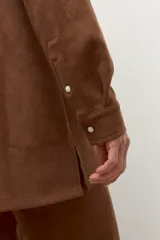 Camisa de manga larga color tostado, con cuello camisero y botones frontales. Presenta bolsillos de parche en el pecho.