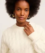 Suéter de punto pesado color crema, con textura trenzada y cuello redondo.
