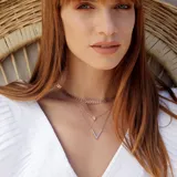 Collar doble con cadena de eslabones color oro rosa. El collar superior tiene un dije triangular con un cristal incrustado y el collar inferior tiene un dije en forma de V.