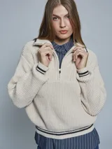 Sweater color crema de tejido grueso con medio cierre, cuello alto y detalles deportivos con rayas negras en puños y hombros.