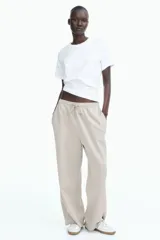 Pantalón deportivo color beige de corte holgado, confeccionado en felpa de algodón liviano con efecto lavado. Cuenta con cintura elástica fruncida, cordón para ajustar, bolsillos laterales discretos y bajos sin rematar.