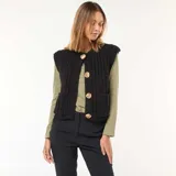 Chaleco de punto grueso color negro, sin mangas, con cuello redondo y cierre frontal con botones dorados.
