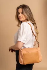 Bandolera de diseño moderno, color beige rosado, con correa regulable y bolsillo frontal con cierre.