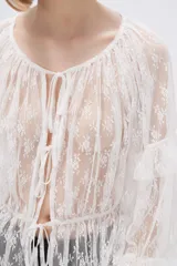 Blusa blanca traslúcida de encaje con mangas largas abullonadas y volados.