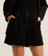 Short negro de corte sastre con cintura alta, trabillas, pliegues, hebillas metálicas y cierre frontal con cremallera.