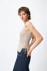 Musculosa de punto color beige, con textura acanalada y detalle de trenzado lateral ajustable.