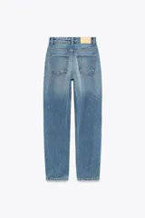 Pantalón de jean gris oscuro, de corte mom fit, tiro alto y largo tobillero. Cuenta con cinco bolsillos, cierre frontal con cremallera y botón.