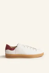 Zapatillas bajas blancas de cuero vacuno con detalle de refuerzo de gamuza color borgoña en el talón y suela de goma color caramelo.
