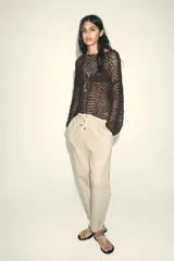 Pantalón color beige de tiro medio con cintura elástica ajustable con cordones, bolsillos delanteros y falsos bolsillos de vivo en la espalda. El bajo es ajustable con botón a presión.
