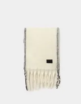 Bufanda tejida color crema con flecos en los extremos y etiqueta de cuero sintético negra.