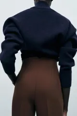 Pantalón marrón de tiro alto con costuras marcadas en delantero y espalda, bolsillos delanteros de vivo y cierre frontal con cremallera, botón interior y gancho metálico.