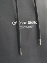 Canguro gris oscuro de manga larga con capucha, fit relajado, bolsillo tipo canguro y estampado en relieve con el texto "(riginals Studi)".