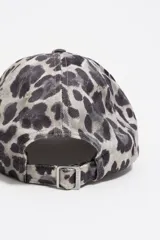 Gorra de béisbol con estampado de leopardo en tonos grises y negros. Presenta un bordado frontal en color celeste claro.