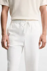 Pantalón de jogging color beige confeccionado en tejido de mezcla de algodón. Cuenta con cintura elástica ajustable con cordón, bolsillos frontales y traseros.
