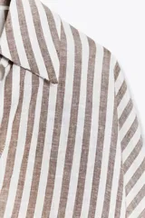 Camisa a rayas verticales color marrón y blanco, de corte holgado, con cuello solapa, cierre frontal con botones y mangas anchas por debajo del codo.