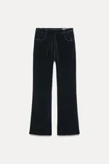 Pantalón de terciopelo negro de tiro medio, con bolsillos delanteros y traseros, pierna recta y cierre frontal con cremallera, botón y gancho metálico.