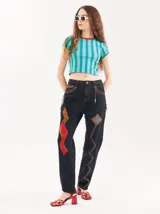 Pantalón de denim negro con parches de colores, tiro alto, corte mom-fit, apliques de cuero trenzado y canutillos alrededor de los bolsillos frontales.