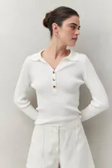 Sweater blanco de punto acanalado con cuello tipo polo y botonadura frontal de botones metálicos. Mangas largas con terminación en pequeñas aberturas.
