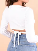 Blusa blanca de mangas largas con escote en V y abertura en el abdomen unida por un aro metálico.