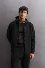 Sudadera con capucha color marrón topo, de corte regular fit, confeccionada en tejido técnico compacto de algodón con elasticidad. Cuenta con cuello subido, manga larga con bolsillo, bolsillos frontales con cierre de cremallera y acabados con rib del mismo tejido.