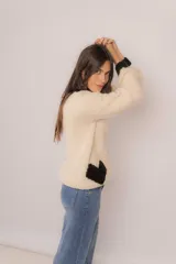 Sweater tejido de lana merino color crema, con cuello redondo y puños negros. Tiene un corazón negro en el frente.