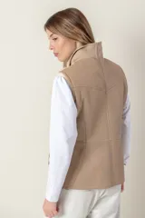 Chaleco color beige con cuello alto y cierre frontal con cremallera. Presenta detalles de piel sintética color crema en los hombros.