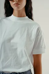 Camiseta blanca de algodón orgánico con cuello redondo alto y mangas cortas dobladas. Presenta un pequeño logo bordado en el pecho.