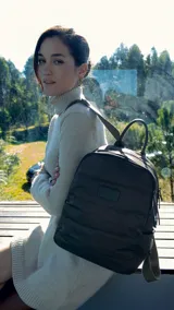 Mochila capitoneada color verde oscuro de nylon, con apertura superior con cierre y tiradores metálicos, bolsillos internos, bolsillo con cierre metálico al frente, correa corta de mano y correas de galón regulables para colgar en la espalda.
