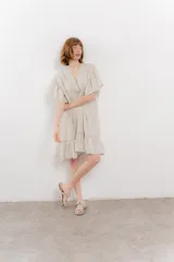 Vestido corto color beige confeccionado en algodón, con escote en V con detalles bordados, mangas cortas amplias con volados y falda con ruedo en volado.