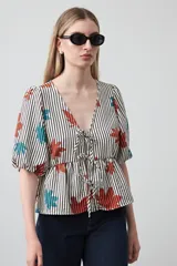 Blusa de silueta relajada con estampado de lunares negros sobre fondo crema. Cuenta con escote en V con lazos regulables, frunce bajo el busto y mangas cortas con volumen.
