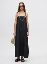 Vestido midi de denim negro, con tirantes finos ajustables y corte holgado. Presenta un ruedo con un volante o semi-pollera.