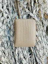 Billetera pequeña de cuero color beige con textura croco, forrada, con cierre metálico y pulsera de cuero.