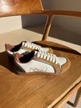 Championes urbanos de cuero color blanco hueso con detalles en marrón. Presentan cordones de algodón color crudo y logo bordado en el lateral.