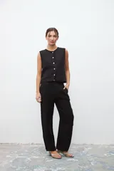 Chaleco negro sin mangas con cuello redondo y cierre frontal con botones blancos.