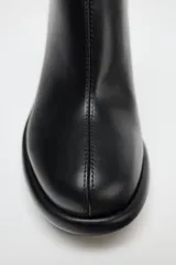 Botín negro de cuero sintético con plataforma y tacón de cuña. Cierre mediante cremallera lateral y acabado en punta redonda.