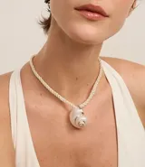 Collar corto con cordón torcido color crema y colgante grande de caracola con detalles dorados.