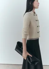 Chaqueta color crema de tejido de punto de canalé, con cuello camisero, cierre de botones en la parte delantera y manga larga.