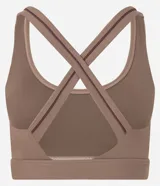 Top deportivo femenino color marrón, con escote redondo y tiras elásticas cruzadas en la espalda. Presenta un pequeño logo bordado en el centro del busto.