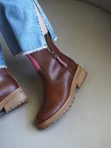 Botas cortas de cuero color marrón con cierre de cremallera lateral y detalle de ribete rosa.